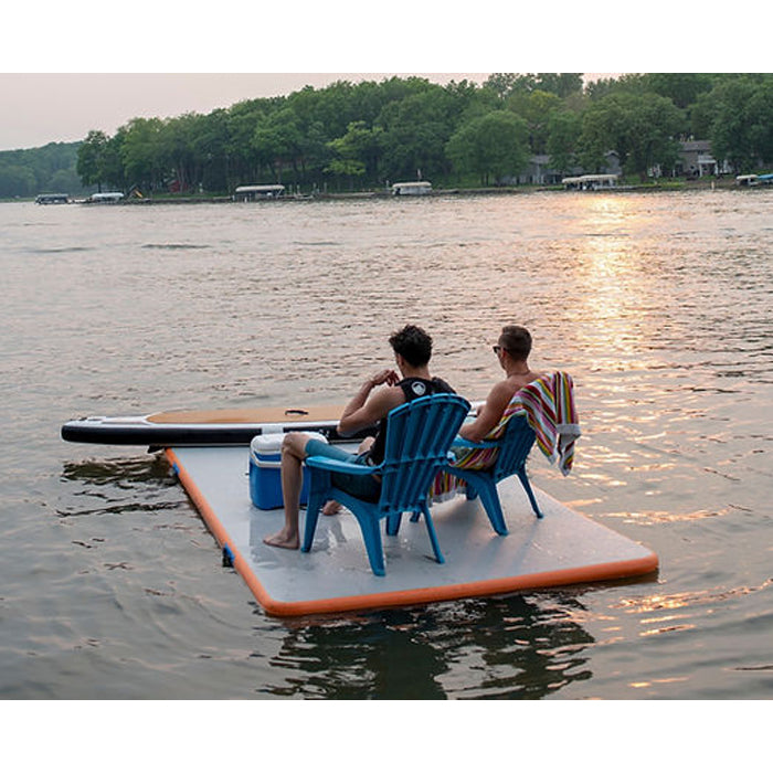 Paradise Pad 6'x13' Inflatable Water Mat with 2 people on plastic chairs sitting on top of the mat with an ice cooler and enjoying the sunset